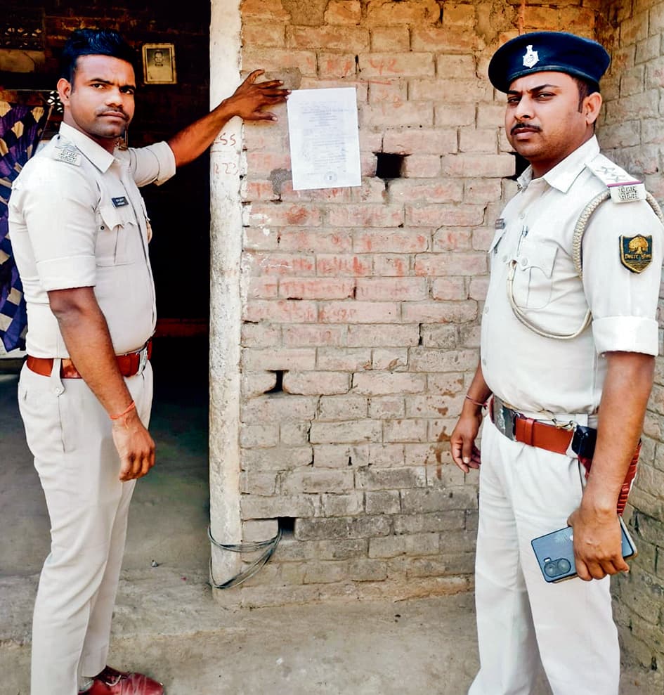 फरार चल रहे अभियुक्त के घर पुलिस ने चिपकाया इश्तेहार