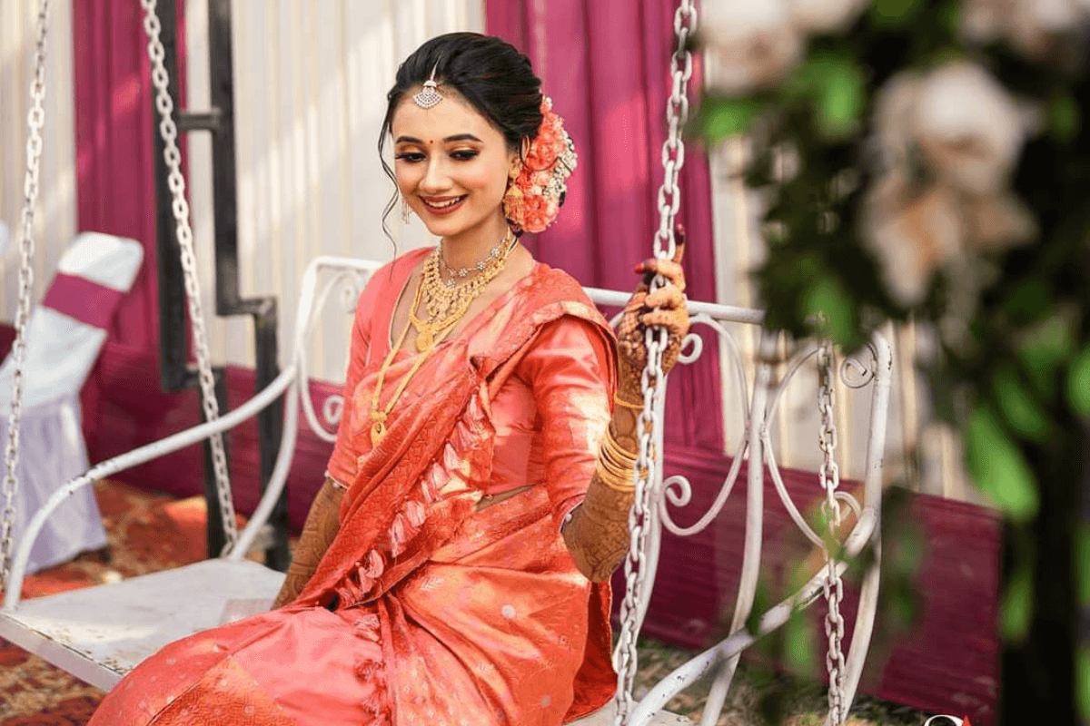 Traditional Teej photoshoot of woman sitting on swing in lehenga suit smiling gracefully.