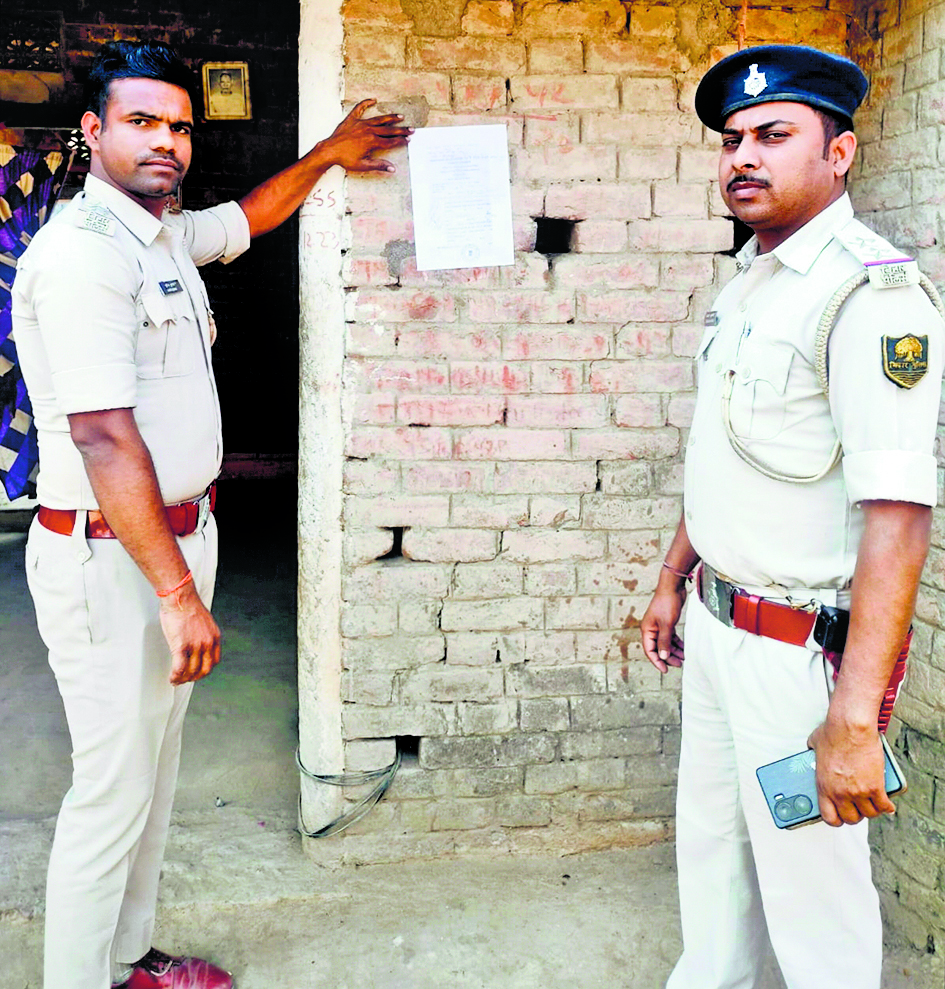 फरार चल रहे अभियुक्त के घर पुलिस ने चिपकाया इश्तेहार
